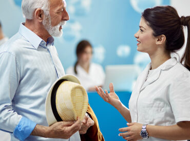 Smiling senior man communicating with a nurse while standing in a lobby at medical clinic.