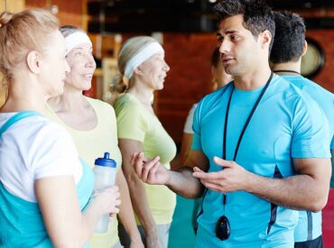 Young sports physician in activewear consulting one of senior women during break between workouts
